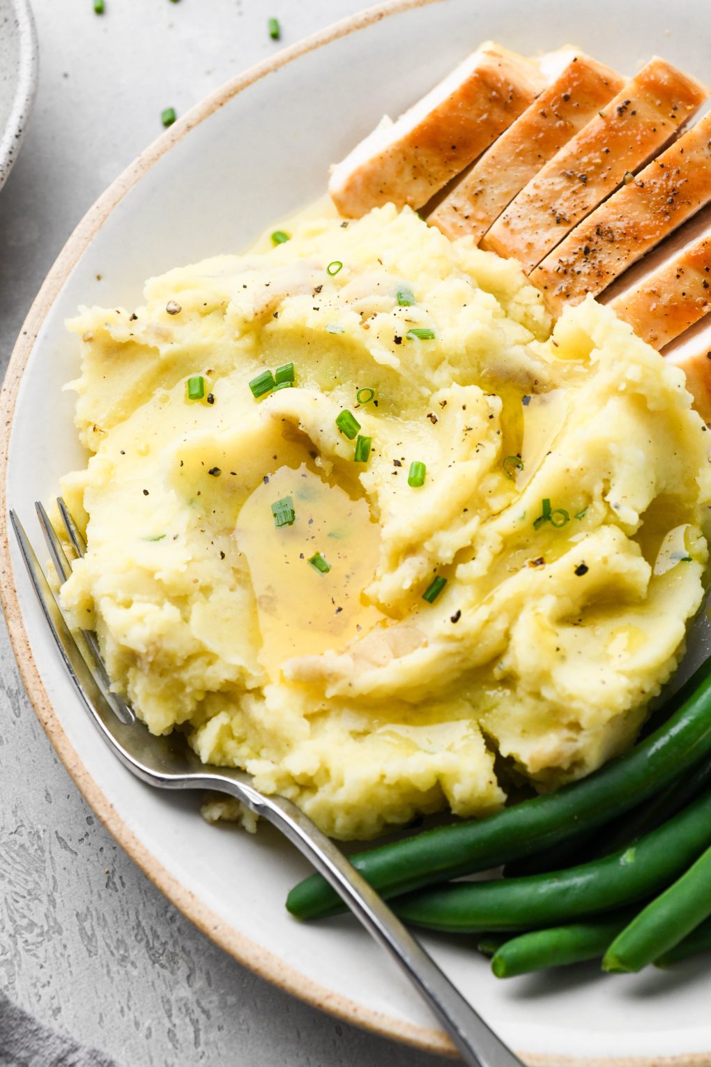 Overhead view of a portion of Whole30 mashed potatoes topped with melted ghee and fresh herbs, on a plate next to green beans and sliced turkey.