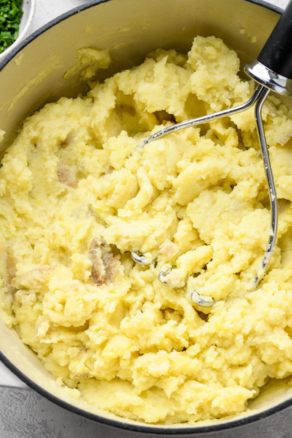 Photos showing how to make Whole30 mashed potatoes - Potatoes being mashed with a potato masher.