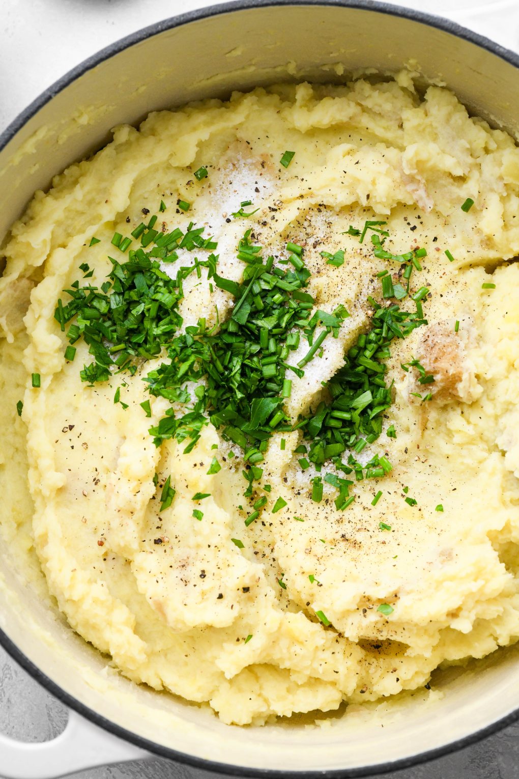 Photos showing how to make Whole30 mashed potatoes - Mashed potatoes in large pot topped with fresh herbs, salt, and pepper.
