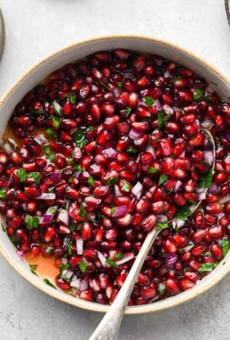 How to make fresh pomegranate relish - An overhead image of a wide shallow bowl of fresh pomegranate relish with diced red onion and parsley.