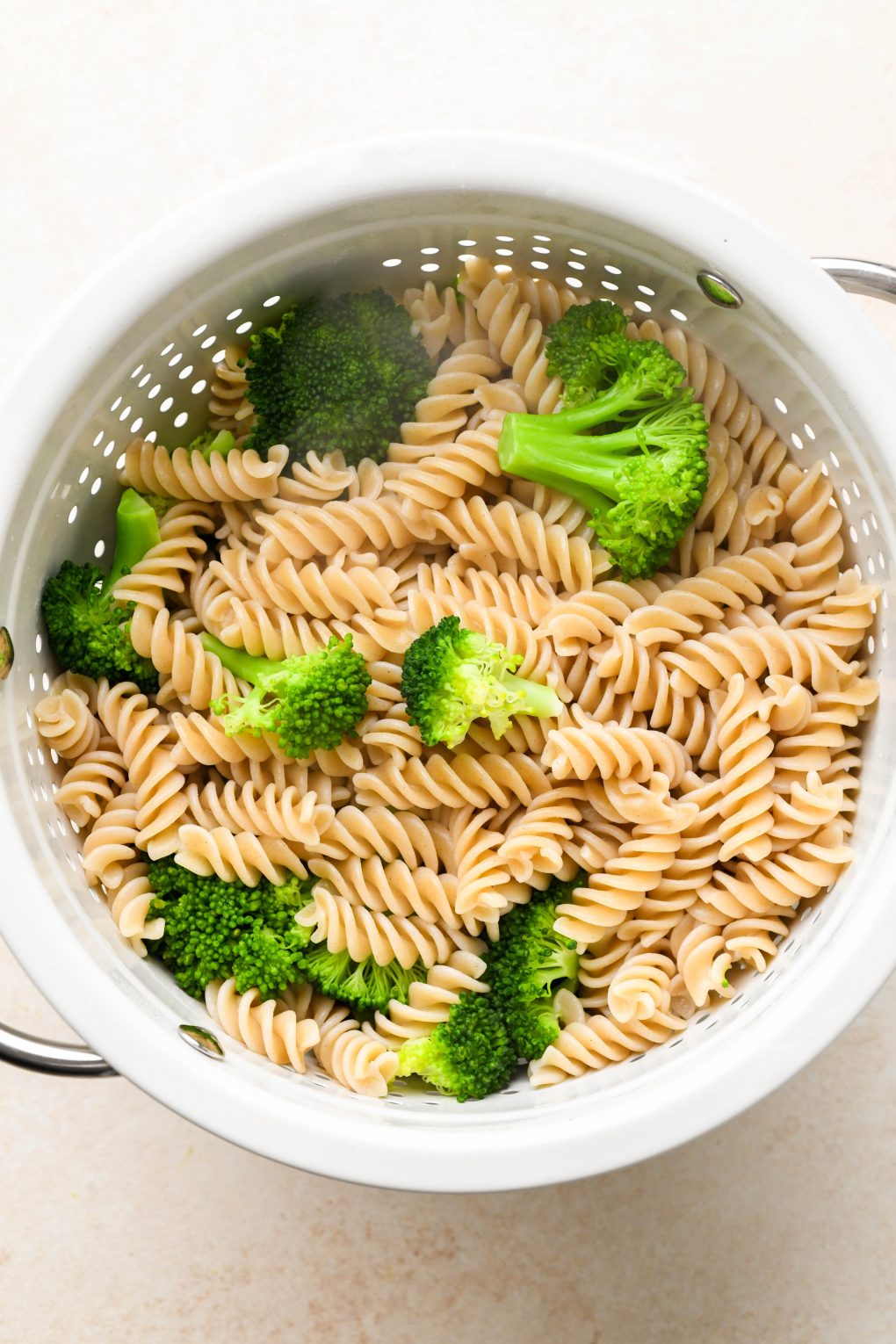 How to make healthy chicken sausage pasta: Cooked pasta and broccoli drained in a white colander.