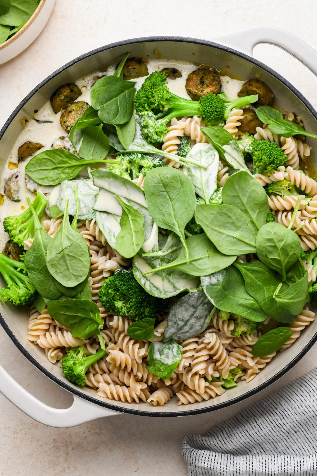 How to make healthy chicken sausage pasta: All ingredients added to skillet with raw baby spinach on top of the pasta and sauce.