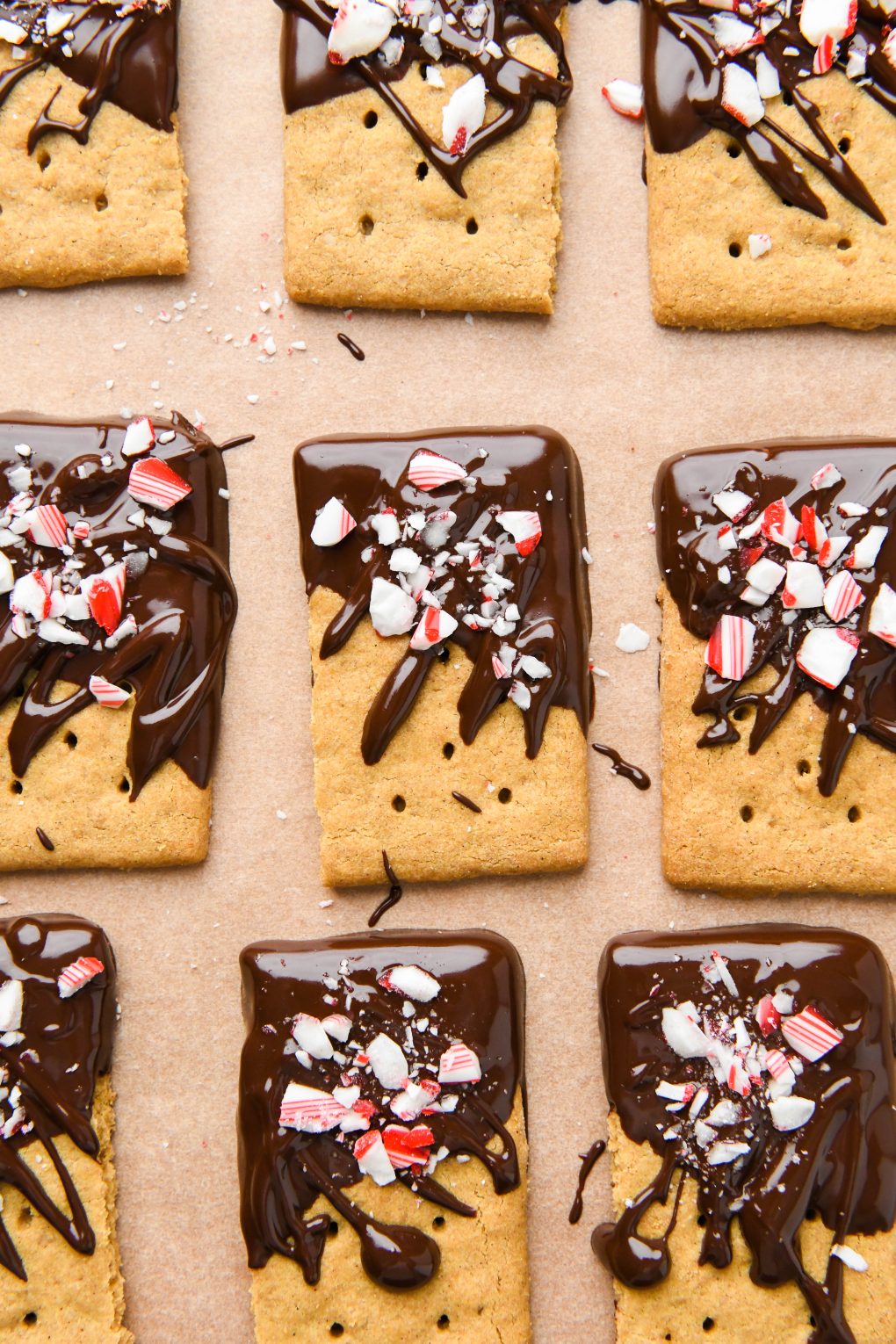 Chocolate dipped graham crackers topped with crushed candy canes on a parchment lined surface.