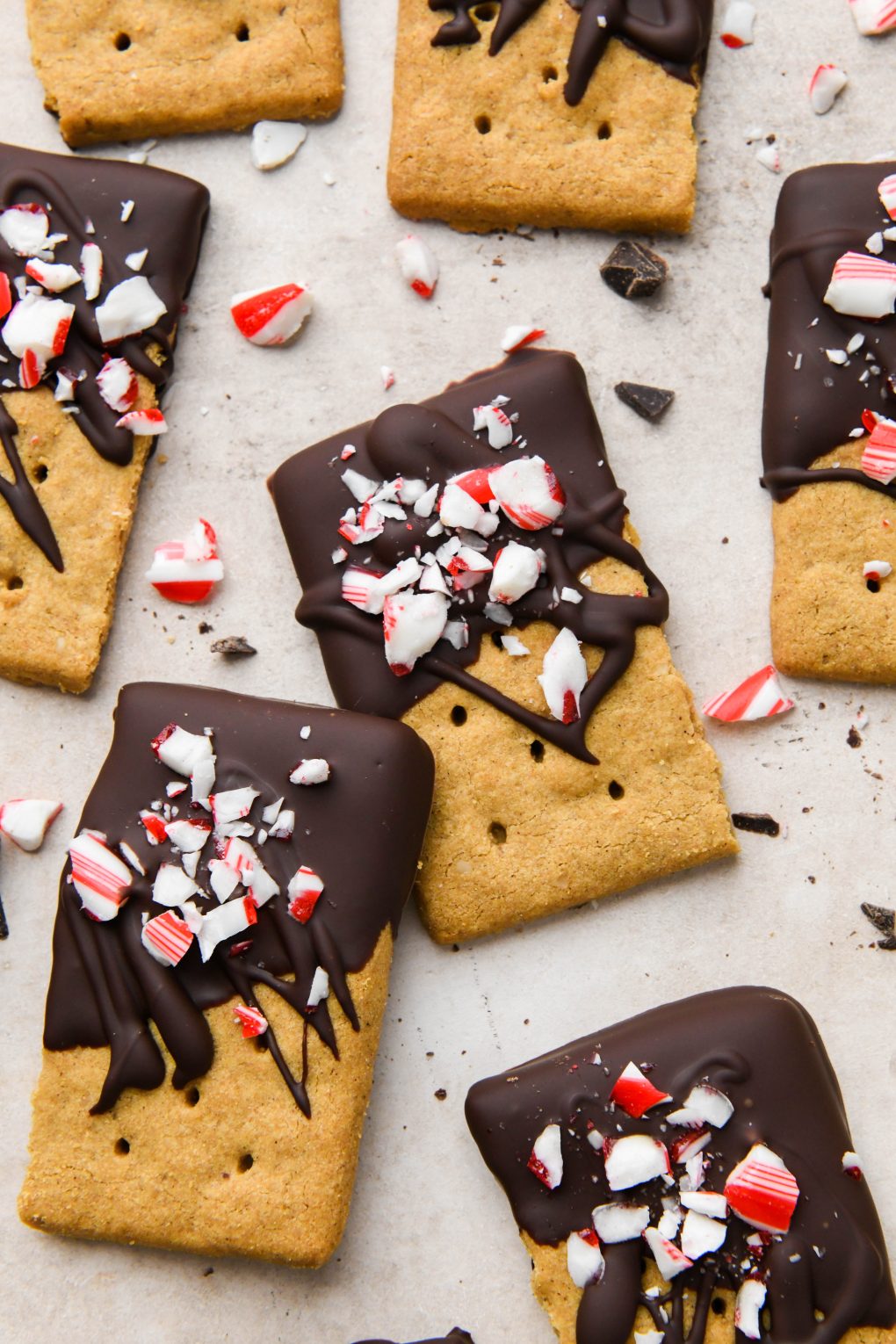 Chocolate dipped graham crackers topped with crushed candy canes on a light brown surface.