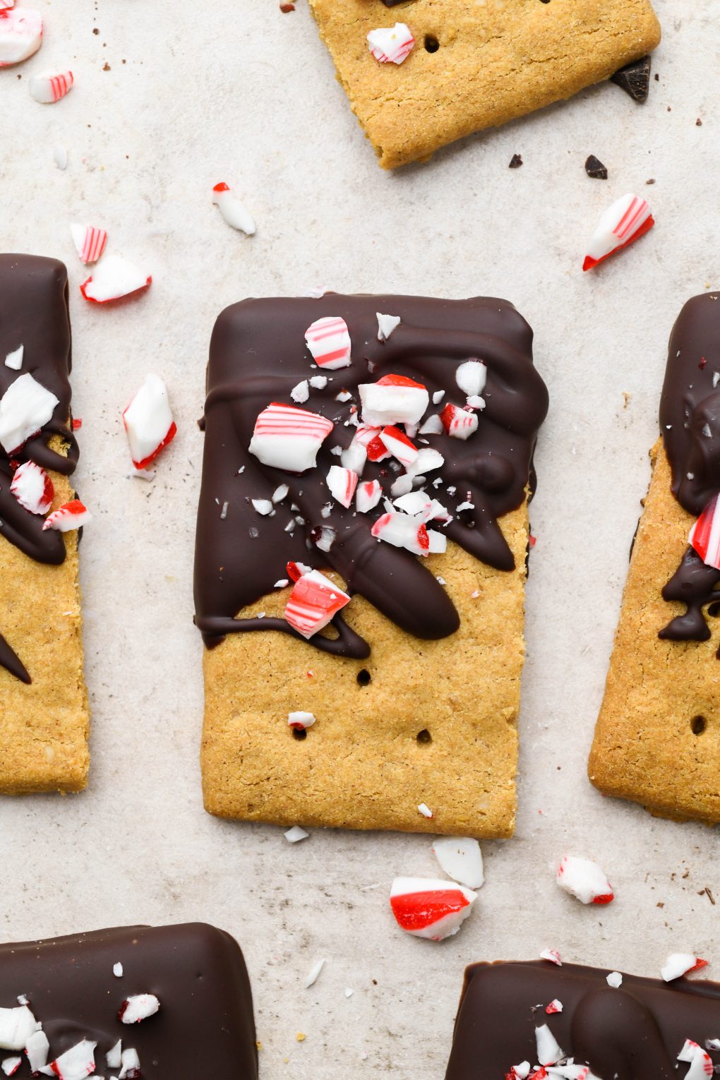 Chocolate dipped graham crackers topped with crushed candy canes on a light brown surface.
