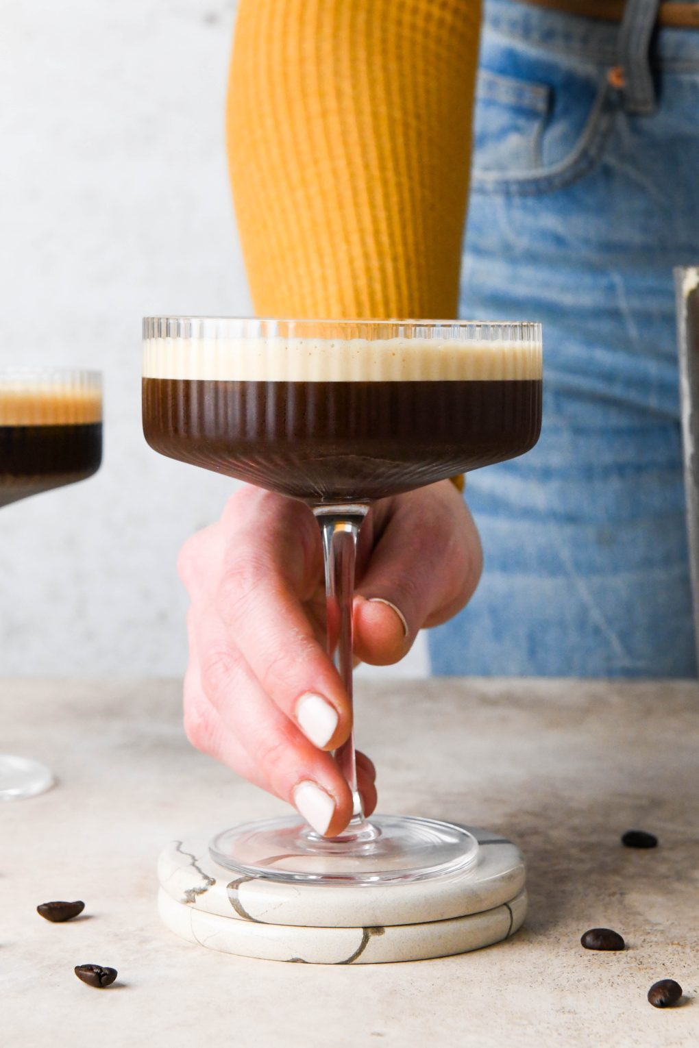 A hand reaching out to grasp the stem of an espresso martini. 