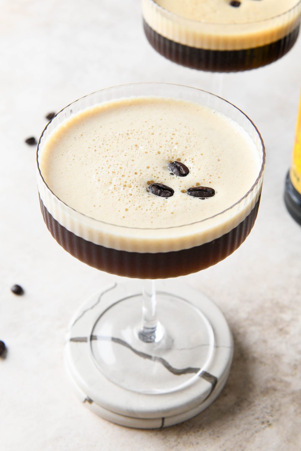 A 45 degree view of an espresso martini topped with 3 coffee beans on a light brown background.