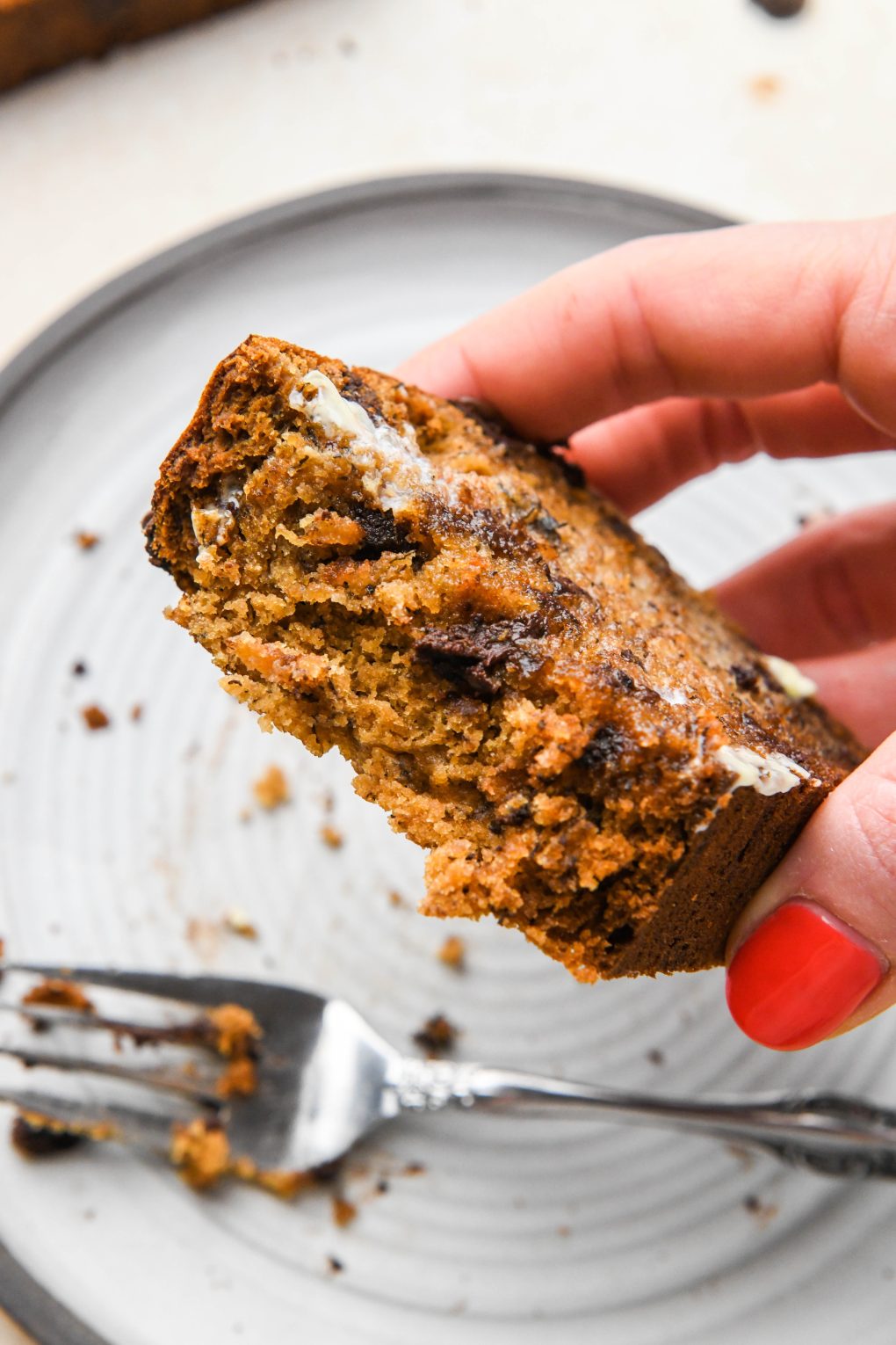 A hand lifting up a slice of banana bread with a few bites take out to show the soft interior.