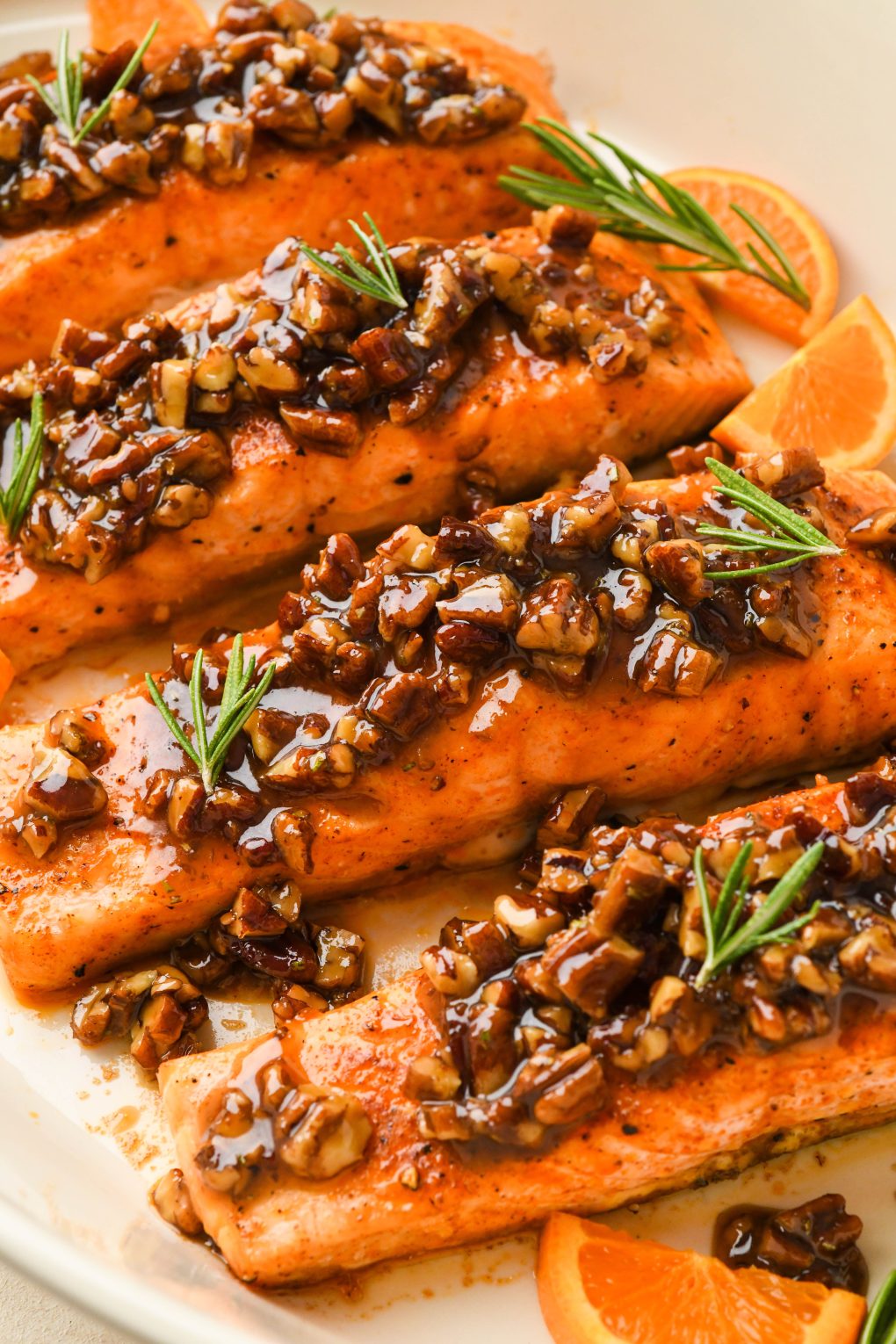 Close up image of oven baked maple pecan glazed salmon fillets in a ceramic baking dish, garnished with fresh rosemary. 