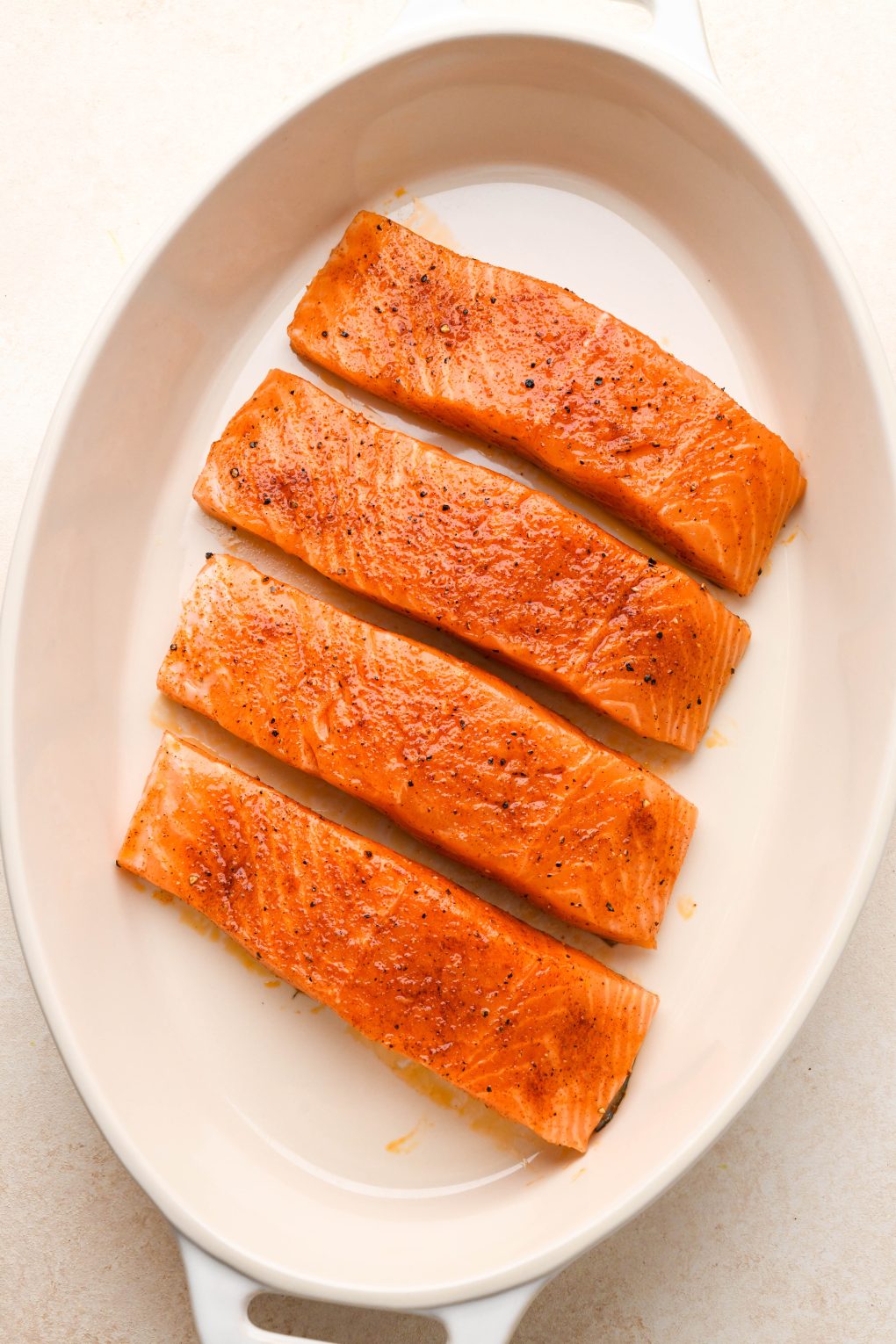 How to make maple pecan glazed salmon: Raw salmon fillets seasoned with coated with olive oil in a ceramic baking dish