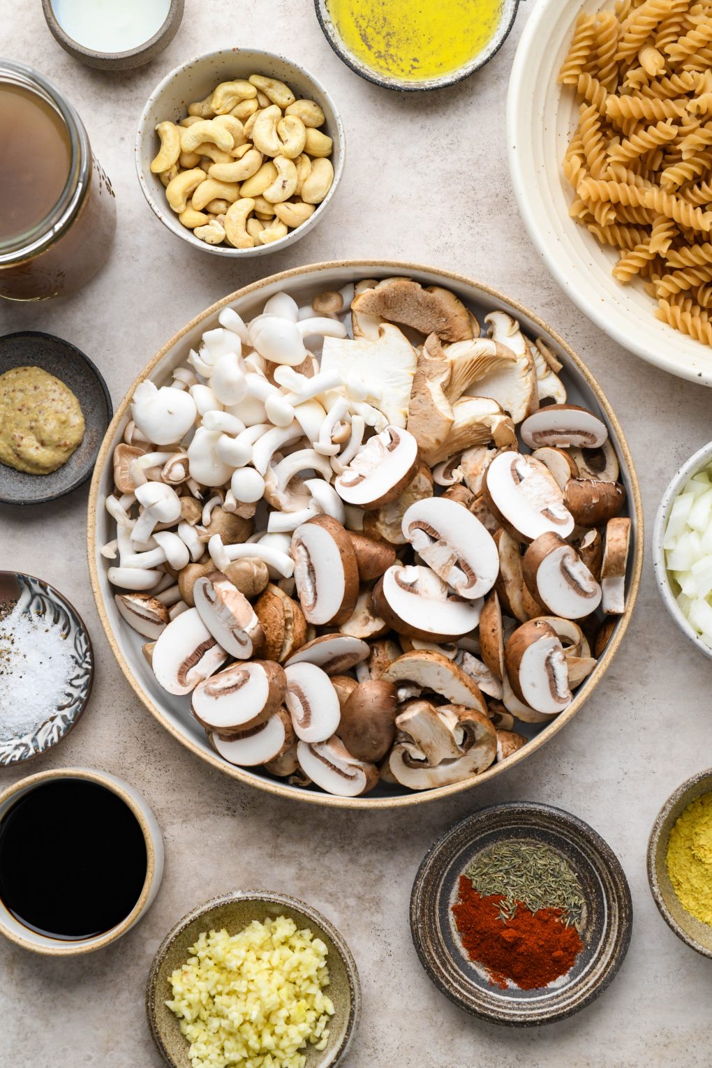 Ingredients for vegan mushroom stroganoff in various ceramic bowls and dishes on a light brown background. 