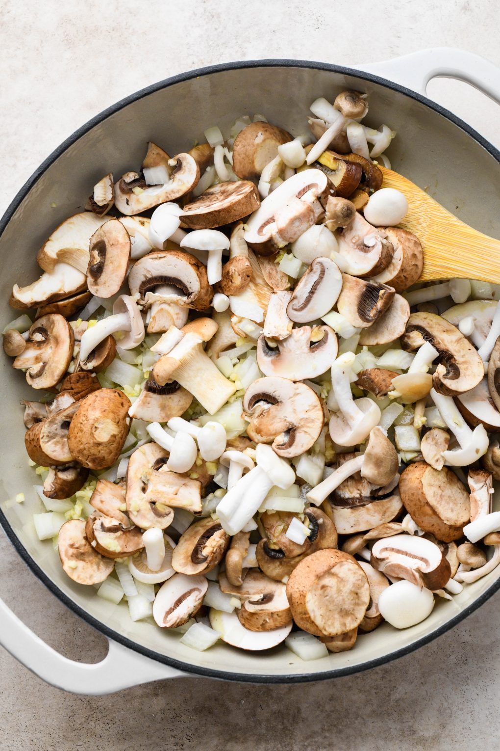 How to make creamy vegan mushroom stroganoff: Raw mushrooms, onion, and garlic in a large ceramic skillet.