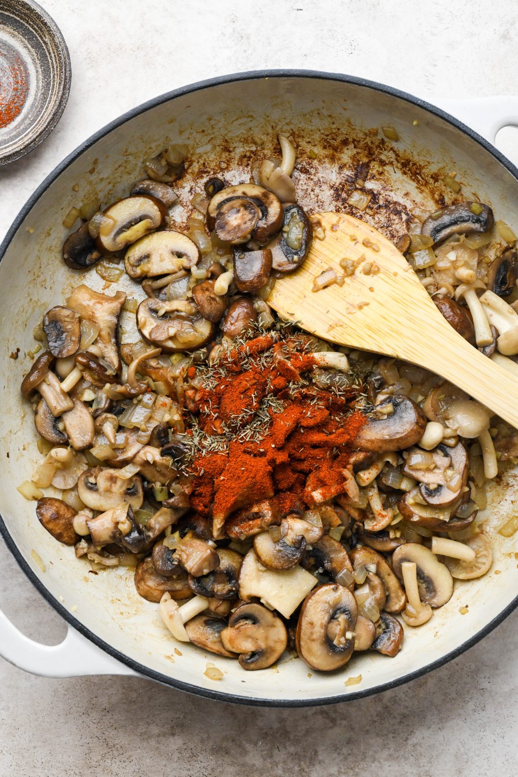 How to make creamy vegan mushroom stroganoff: Cooked mushrooms, onions, and garlic in a large ceramic skillet with paprika and thyme on top of veggies.