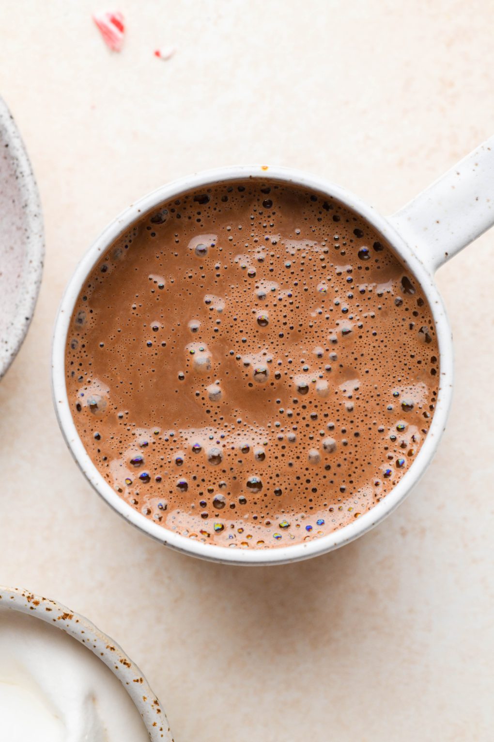 Close up shot of creamy peppermint hot chocolate in a speckled mug on a light brown background. 