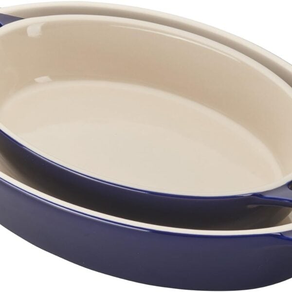 Two oval ceramic baking dishes, one nested inside the other, with a cream-colored interior and dark blue exterior, both featuring handles labeled STAUB.