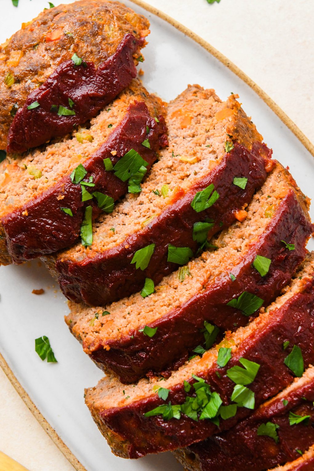 Baked Classic Whole30 Meatloaf cut into slices and topped with fresh parsley on a white ceramic serving platter.