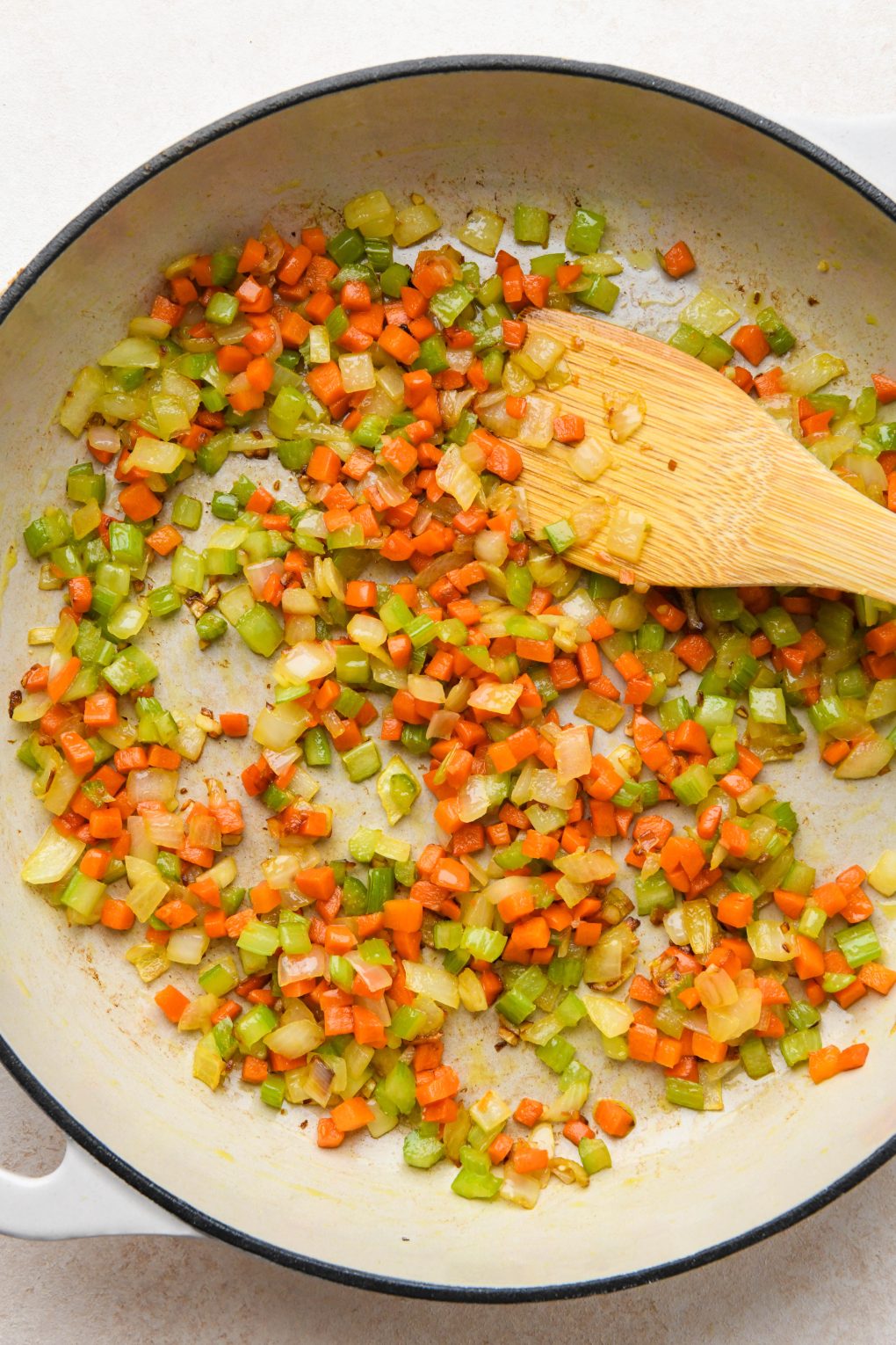 How to make classic Whole30 meatloaf: Sautéing diced onions, carrots, and celery in a large ceramic skillet.