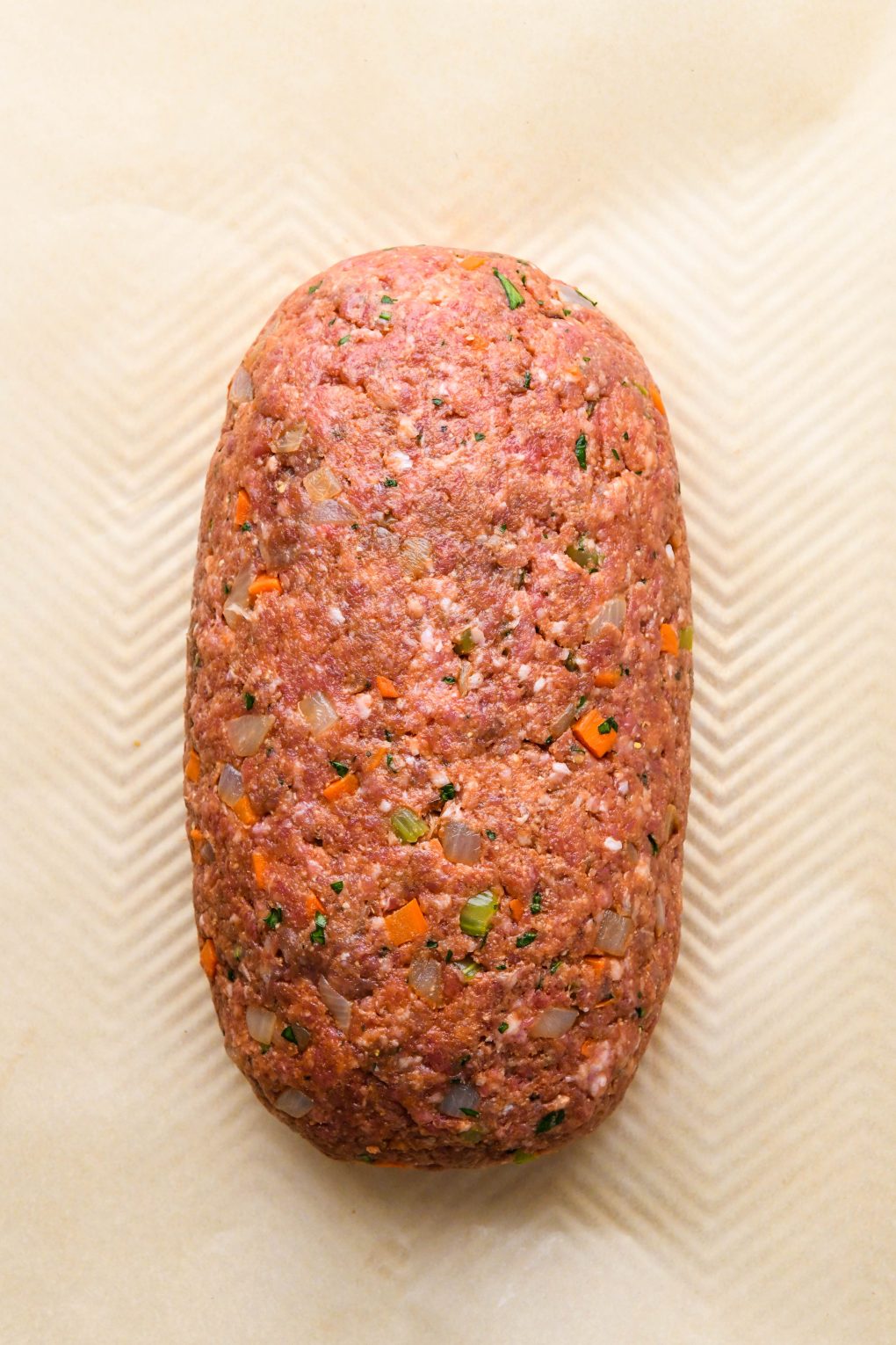 How to make classic Whole30 meatloaf: Raw meatloaf mixture formed into a loaf on a parchment lined baking sheet.