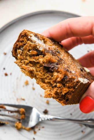 A hand lifting up a slice of banana bread with a few bites take out to show the soft interior.