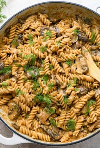 A large ceramic skillet of creamy vegan mushroom stroganoff topped with fresh dill.