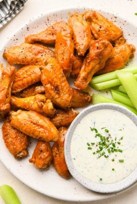 Crispy Baked Buffalo Chicken Wings on a speckled platter with celery sticks and a small bowl of creamy ranch dressing.