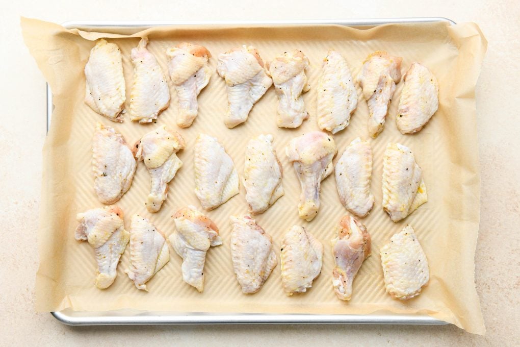 How to make Crispy Baked Buffalo Chicken Wings: Seasoned chicken wings spread out on a large lined baking sheet.