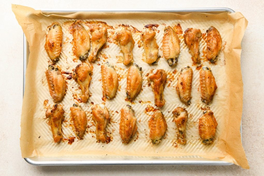 How to make Crispy Baked Buffalo Chicken Wings: Seasoned and baked crispy chicken wings spread out on a large lined baking sheet.