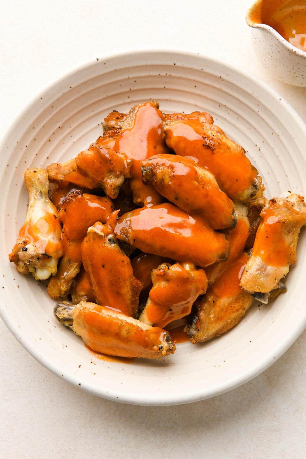 How to make Crispy Baked Buffalo Chicken Wings: Buffalo sauce poured over a bowl of crispy baked chicken wings.