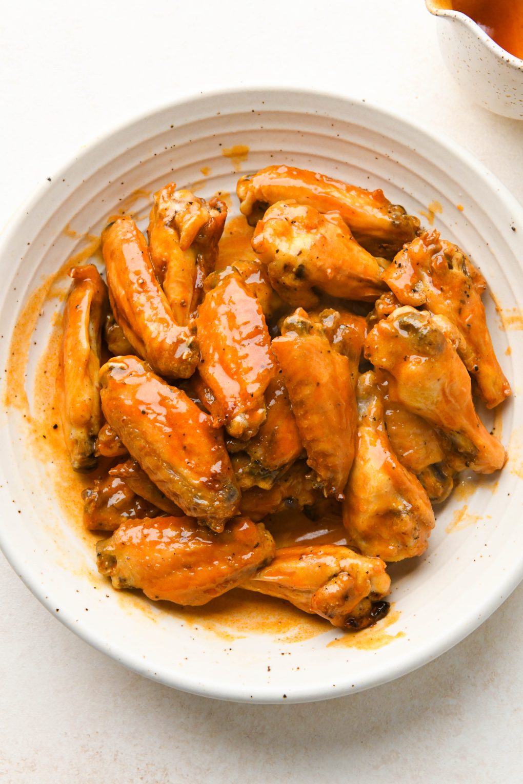 How to make Crispy Baked Buffalo Chicken Wings: Crispy baked chicken wings tossed with buffalo sauce in a large bowl.