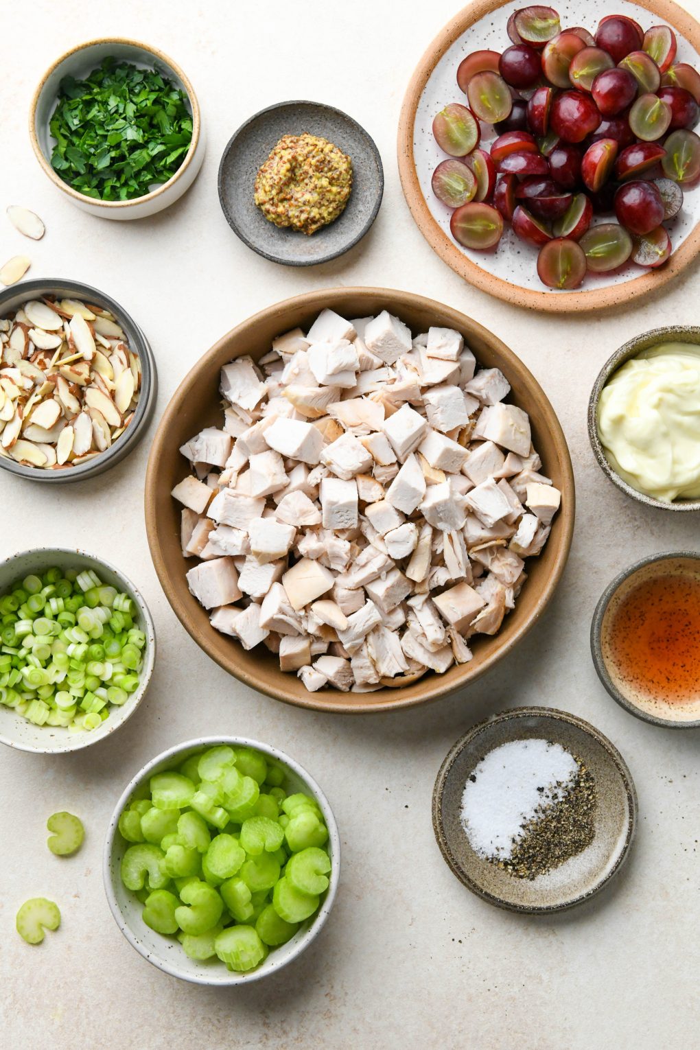 Ingredients for easy chicken salad with grapes in various ceramic plates and bowls on a light cream colored background. 