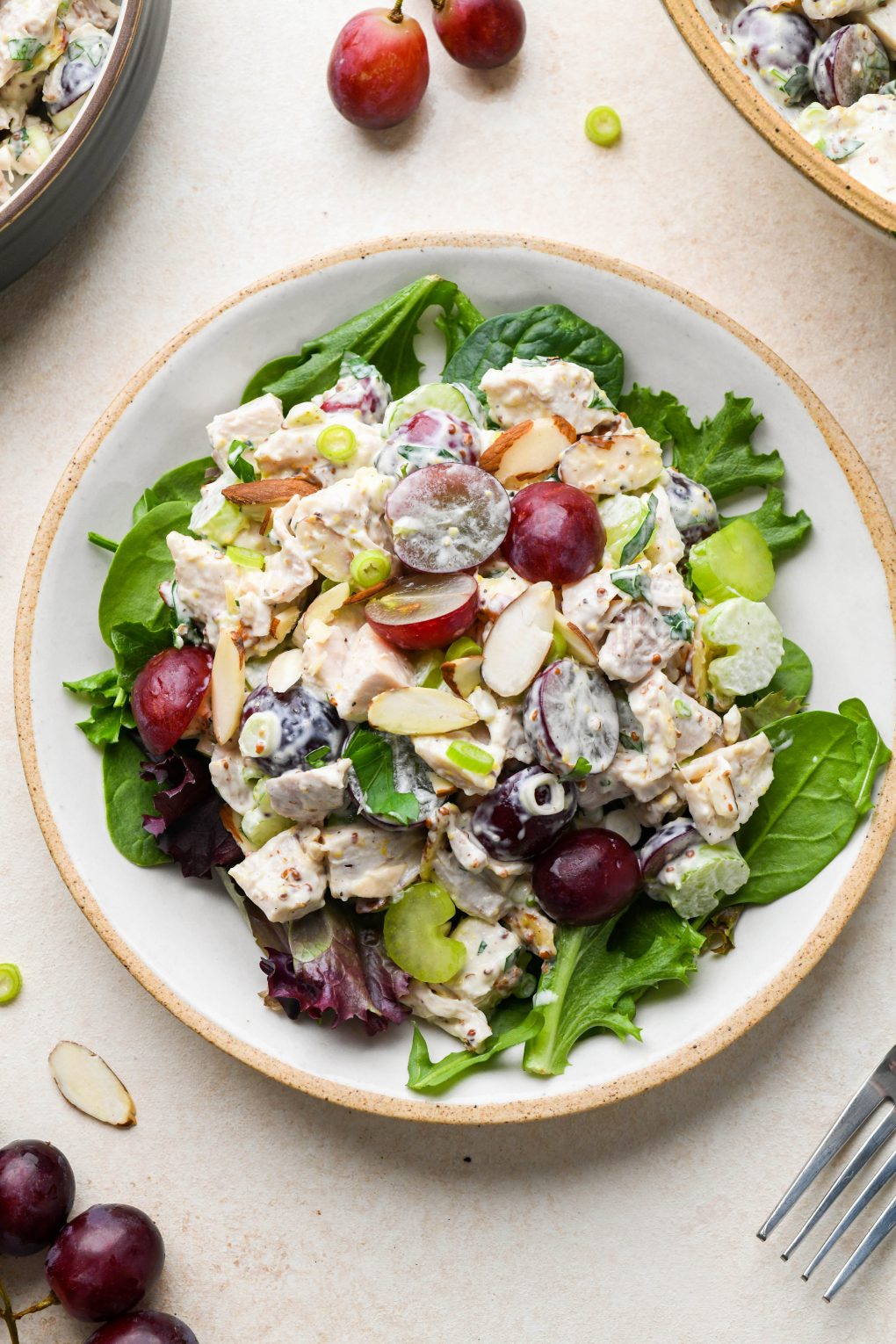 Easy Chicken Salad with Grapes and Almonds on a bed of lettuce on a light colored ceramic plate on a cream colored background.