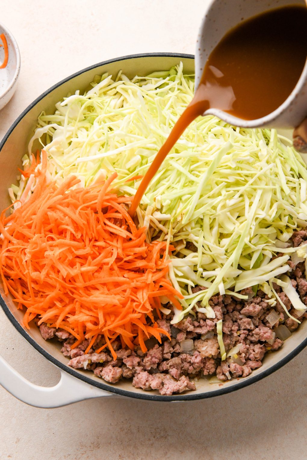 How to make Egg Roll in a Bowl: Sauce being poured in on top of the shredded cabbage and carrots.