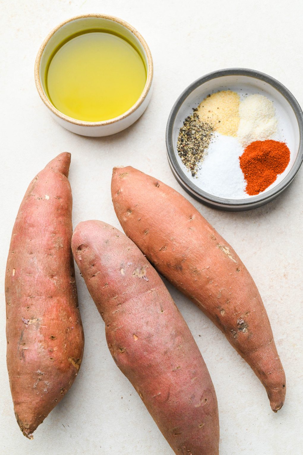 Ingredients for baked sweet potato fries on a light cream colored background.