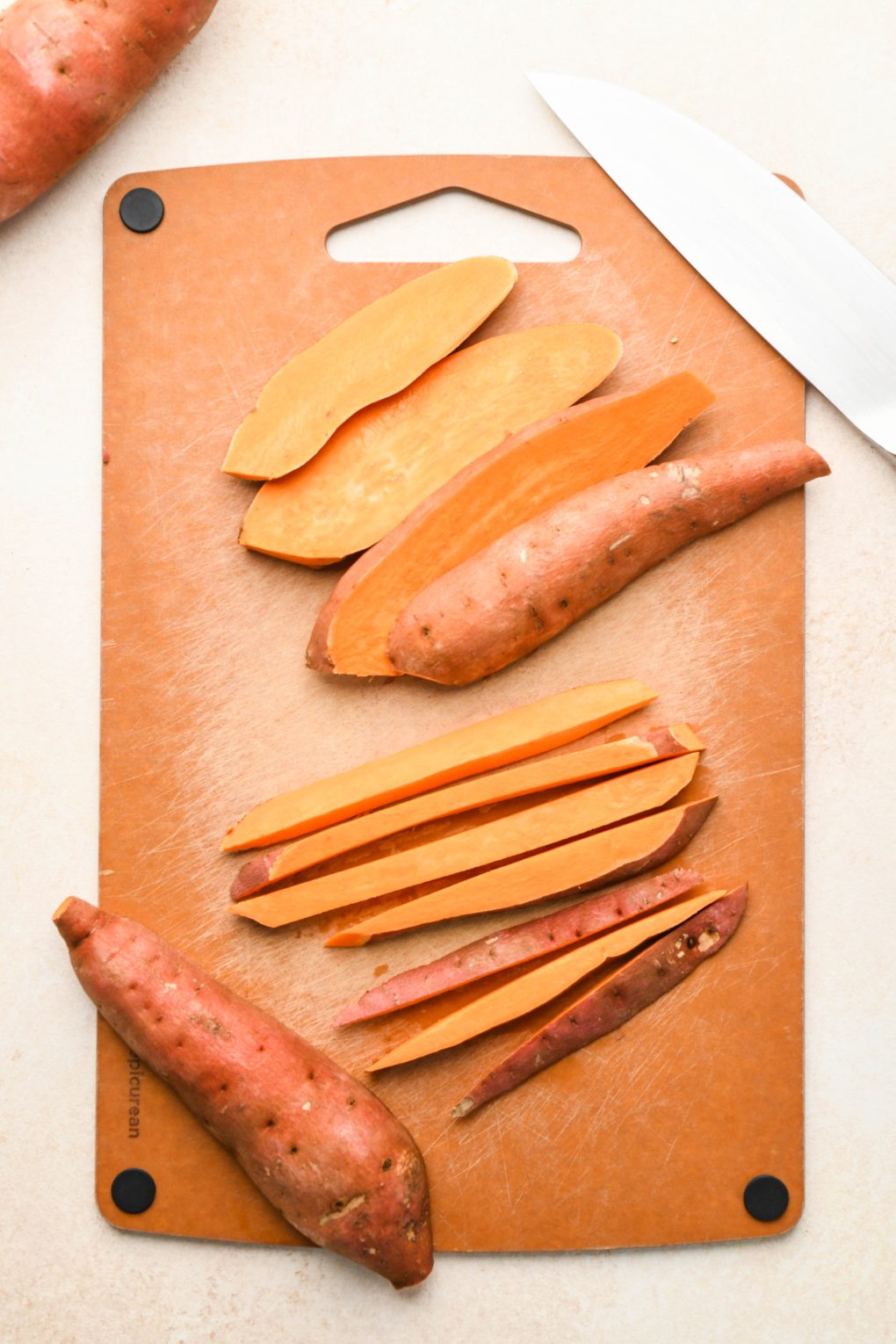 Sweet potatoes on a cutting board being cut into fry sized pieces.