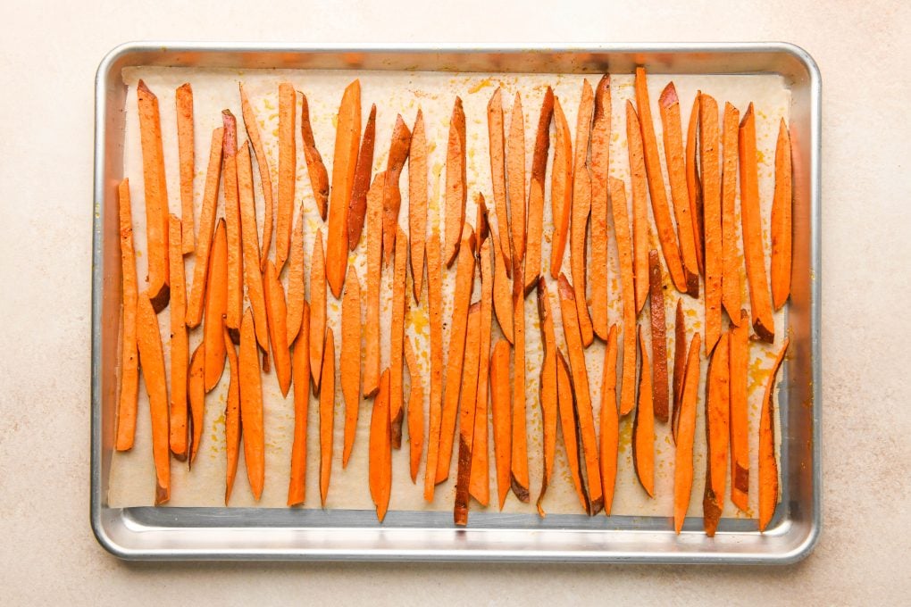 How to make Baked Sweet Potato Fries: Cut sweet potatoes on a large parchment lined baking sheet tossed with oil and spices and spread out in a single layer.