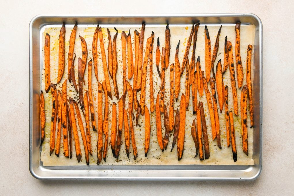 How to make Baked Sweet Potato Fries: Cut sweet potatoes on a large parchment lined baking sheet tossed with oil and spices and spread out in a single layer and roasted until crispy.