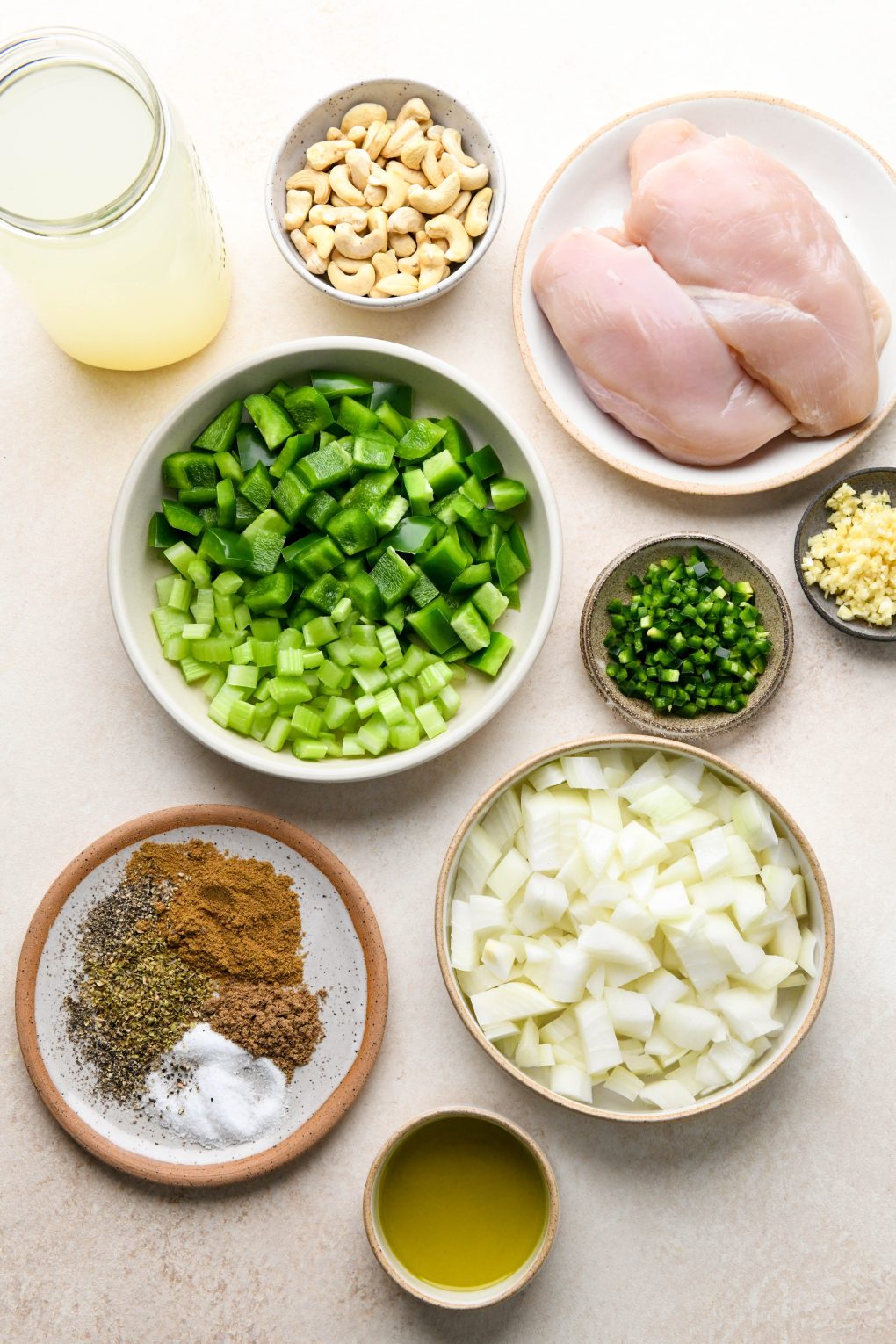 Ingredients for whole30 white chicken chili in various ceramic plates and bowls on a light cream colored background.