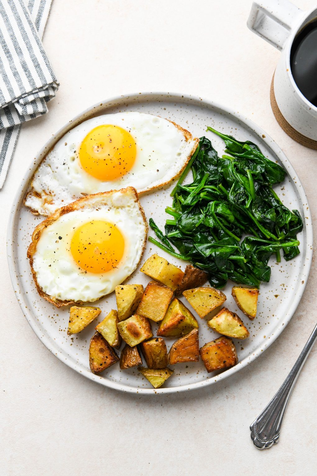 Whole30 breakfast on a speckled plate: Sunny side up fried eggs, sautéed spinach, and roasted potatoes.