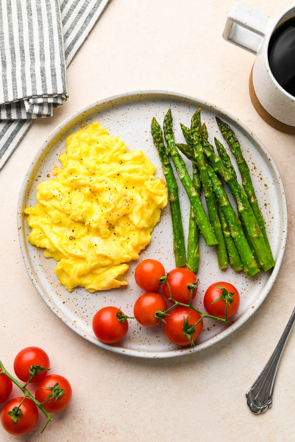 Whole30 breakfast on a speckled plate: Soft scrambled eggs with a side of roasted asparagus and cherry tomatoes.