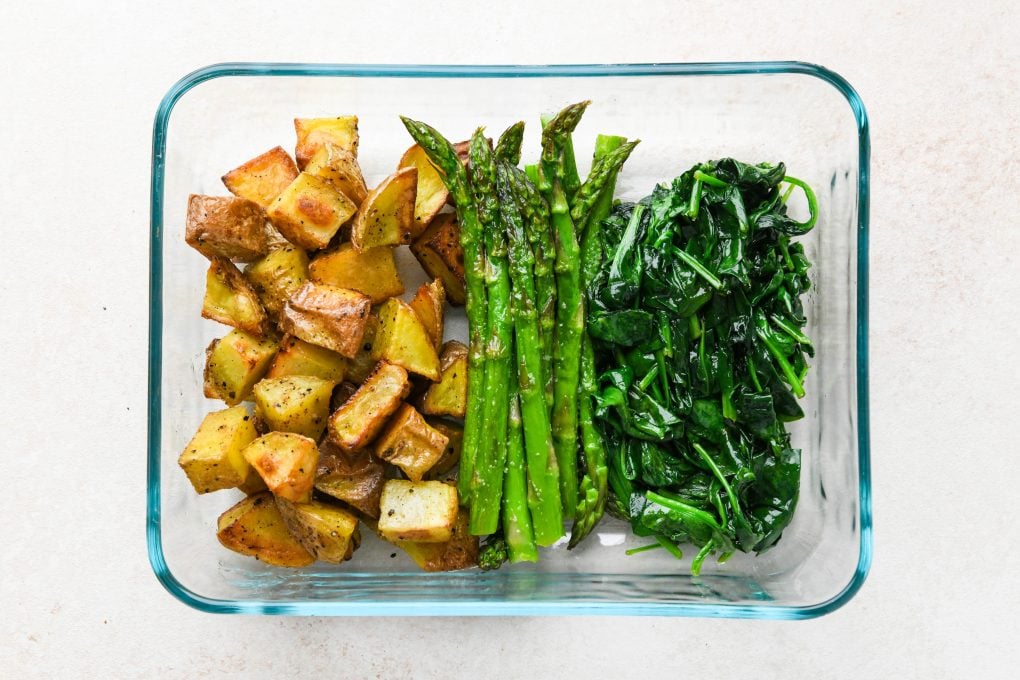 Roasted potatoes, asparagus, and spinach in a glass container for meal prepped breakfasts