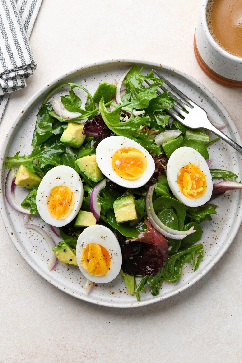 Whole30 breakfast on a speckled plate:Hard boiled eggs over a simple green salad with avocado.