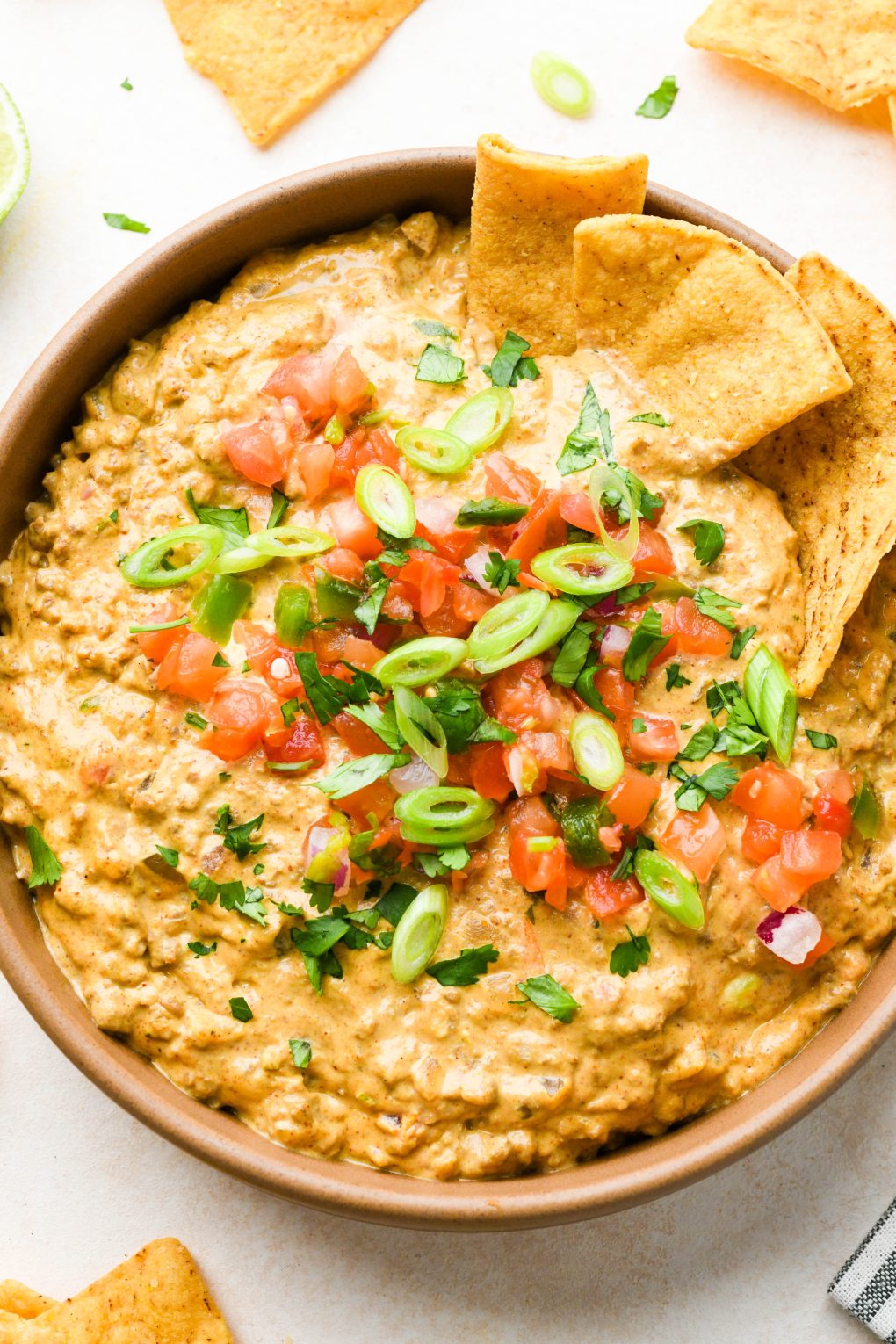 A large ceramic bowl filled with dairy free queso fundido with ground beef, topped with pico de gallo, cilantro, and thinly sliced green onions with some chips dipping into the dip. 