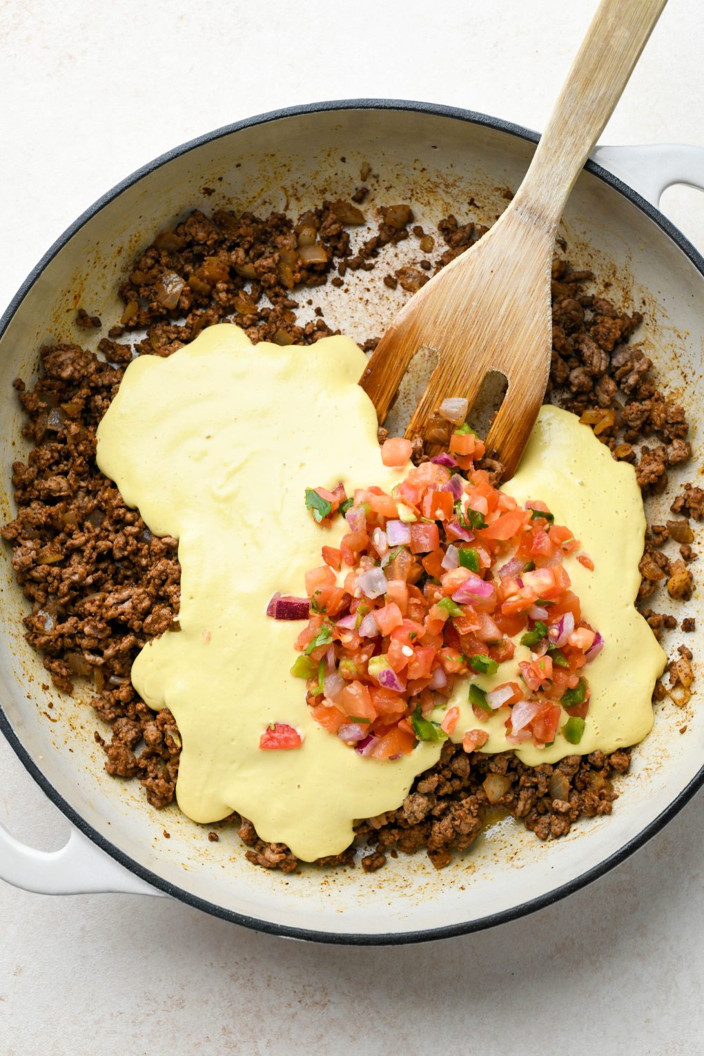 How to make Dairy Free Queso Fundido with Ground Beef: Cooked ground beef and onion in skillet with spices mixed in, cashew queso and pico de gallo on top. 