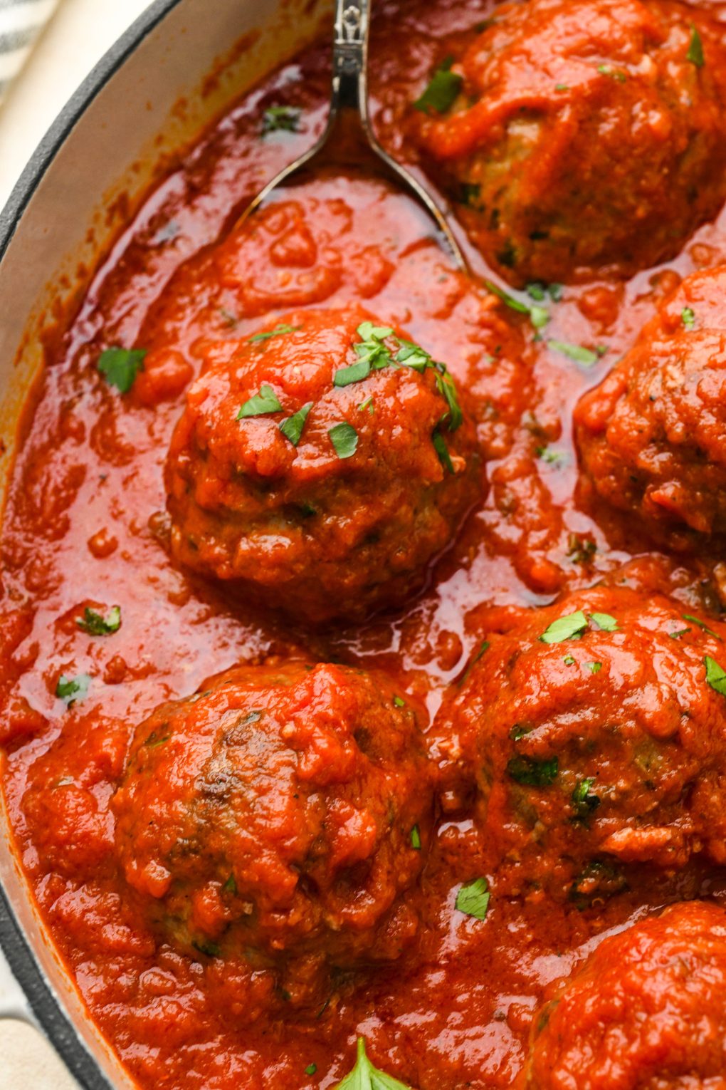 Close up of a gluten free meatball in marinara on a serving spoon in a skillet.