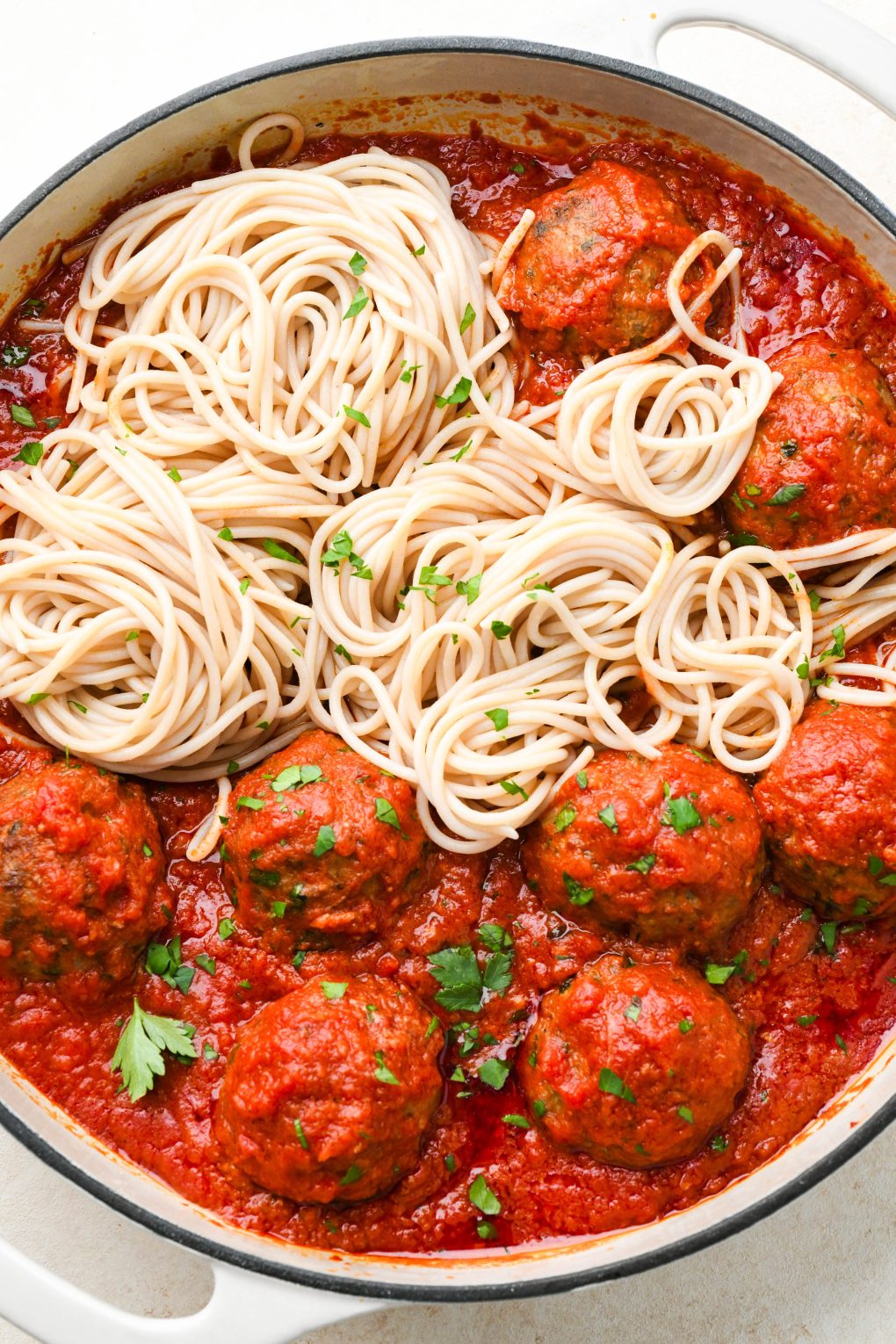 Gluten free meatballs in marinara sauce on one side of a skillet, with spaghetti noodles in the other half of the skillet.