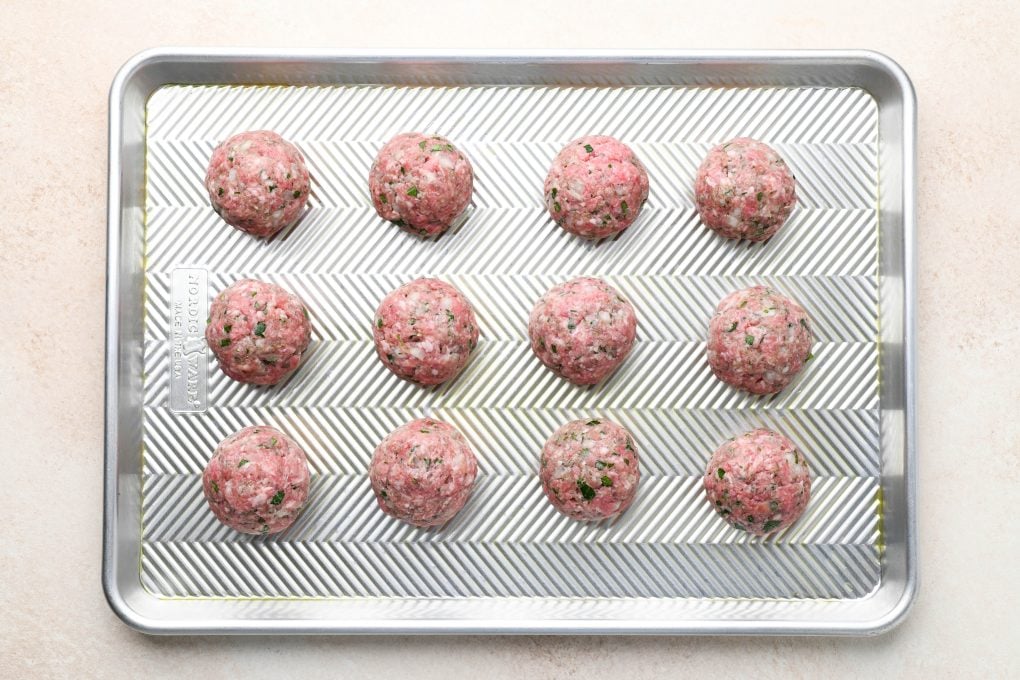 Raw meatballs on a lightly greased baking sheet.
