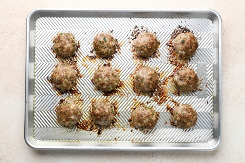 Cooked meatballs on a lightly greased baking sheet.
