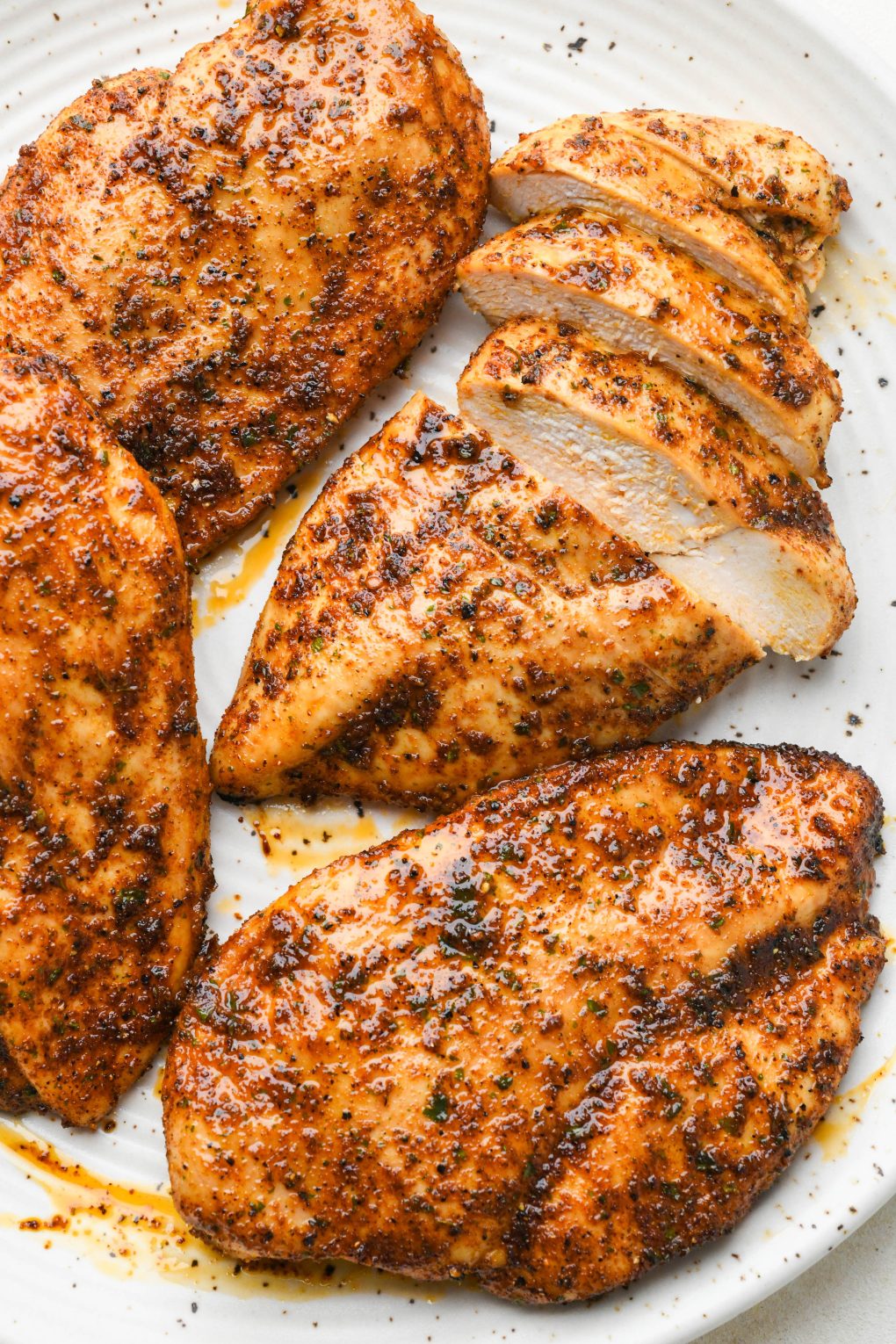 Four oven baked chicken breasts on a large speckled platter, one breast sliced into strips with the juicy interior showing. 