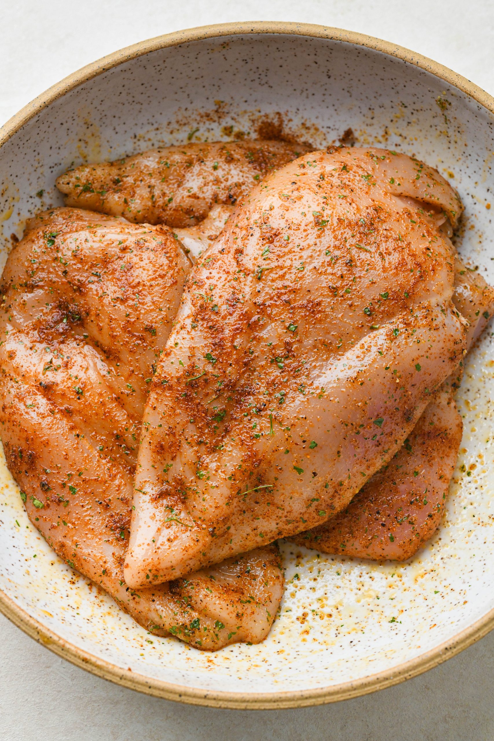 How to make baked chicken breast: Spices and oil evenly coating chicken breasts in a large ceramic bowl