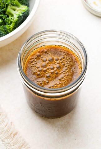 A small mason jar of homemade stir fry sauce next to a bowl of broccoli florets.